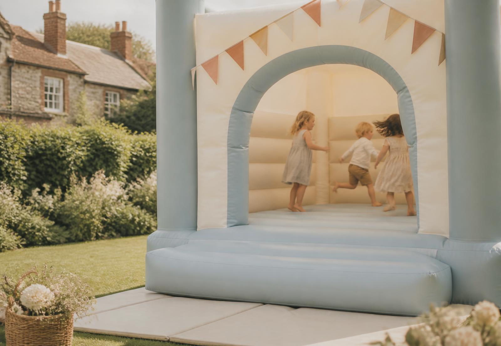 Children playing in a pastel blue and cream bouncy castle in a garden
